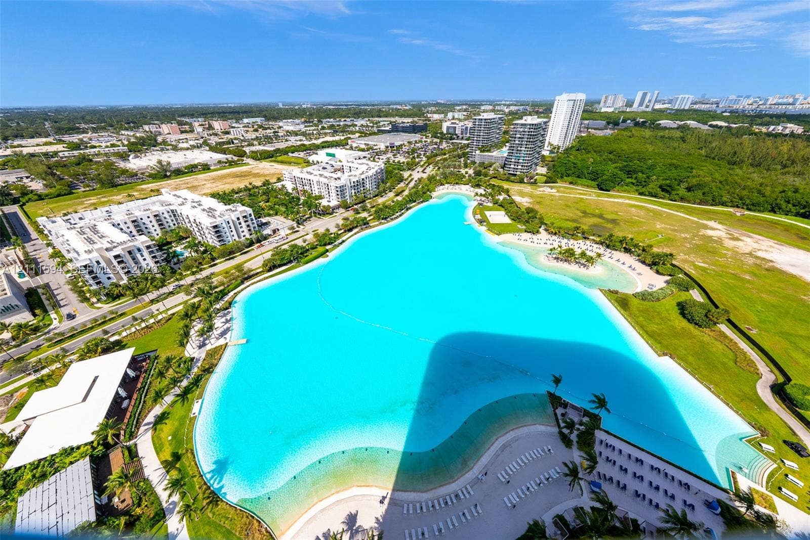 2411 Laguna Circle, #2506, North Miami, FL 33181 Aerial perspective featuring a large crystalline lagoon, expansive sandy shoreline, manicured green space, and paved pathways