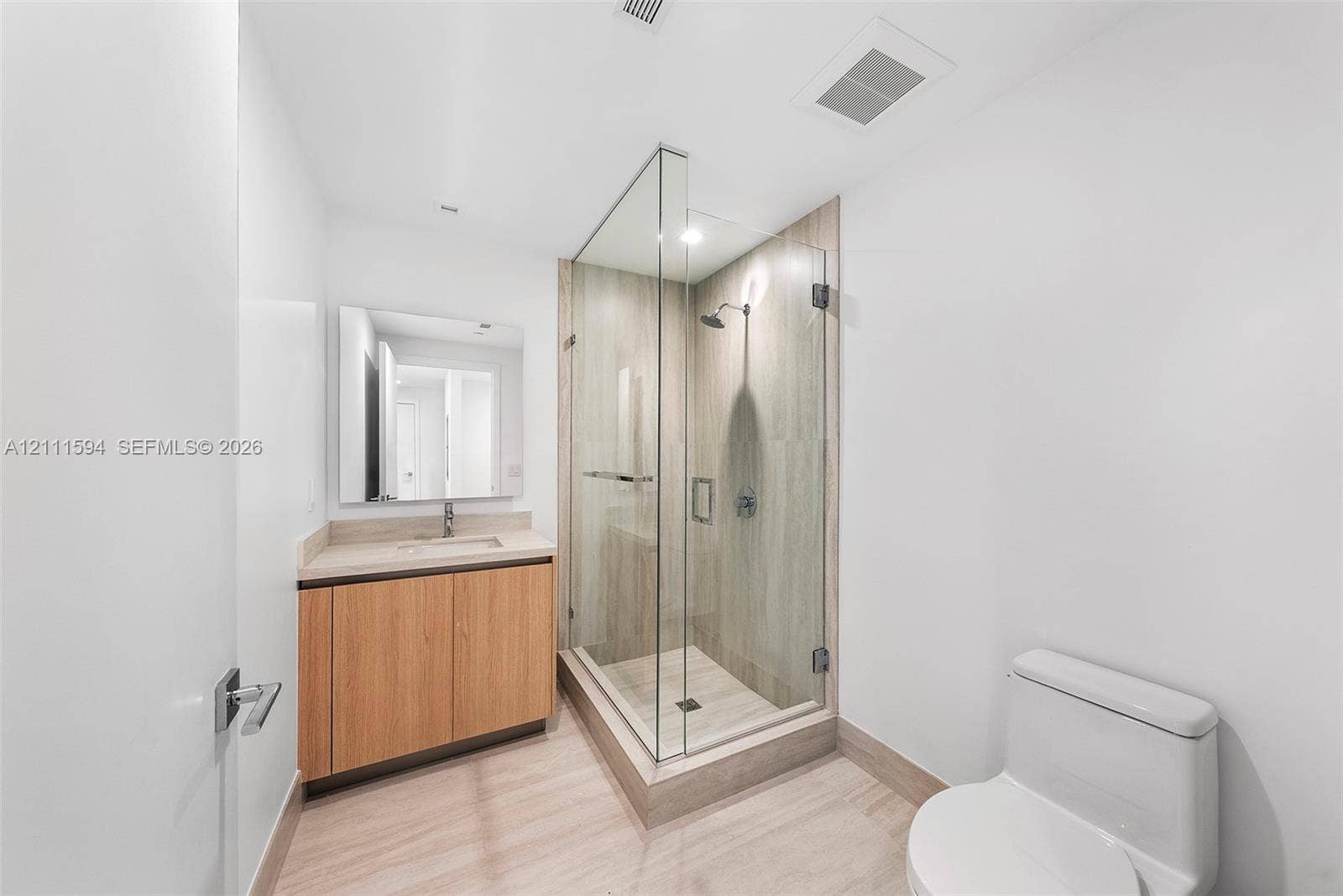 2411 Laguna Circle, #2506, North Miami, FL 33181 Walk-in shower with frameless glass enclosure and tile surround, wood-finish cabinetry, rectangular under-mount sink, and neutral tile flooring