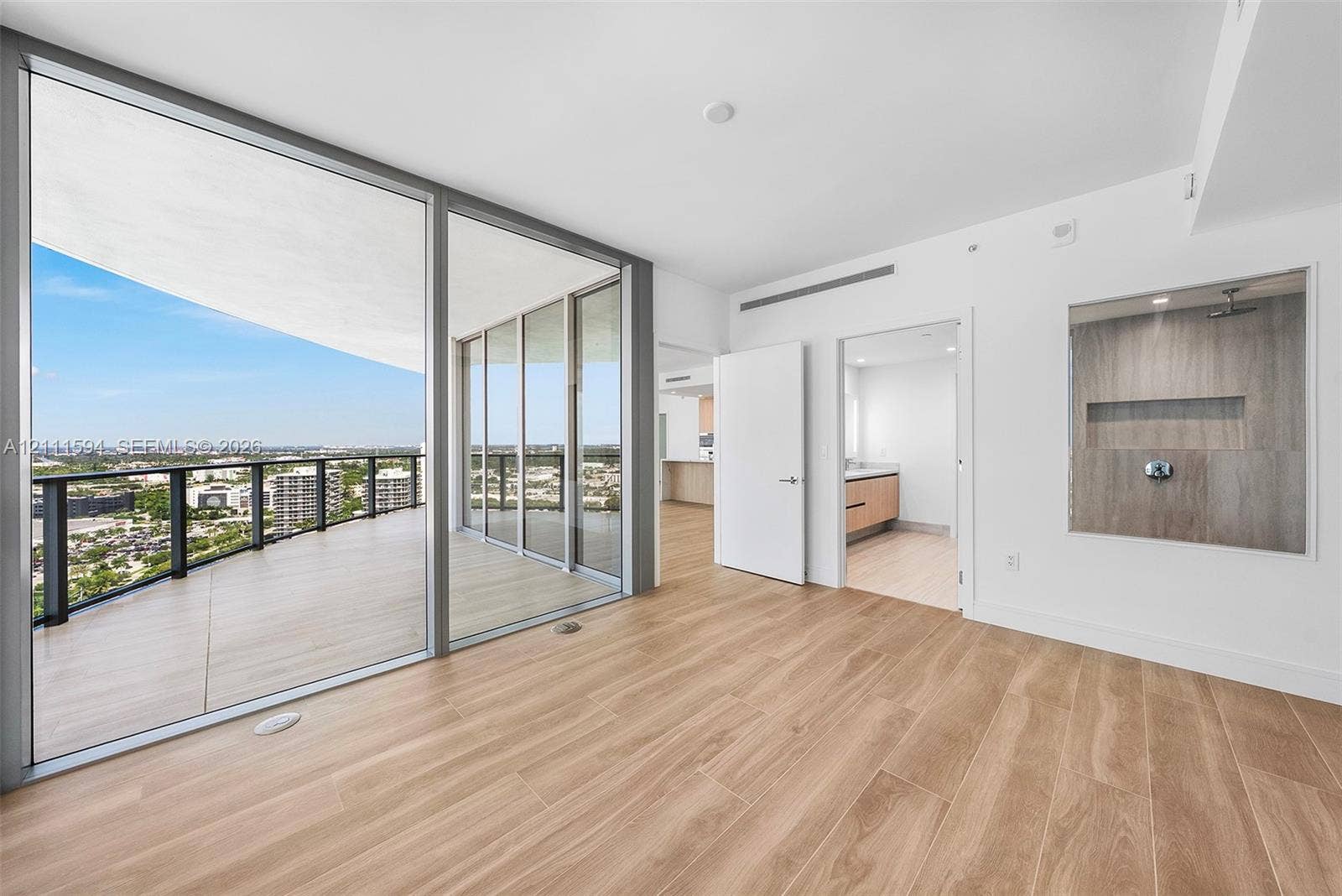 2411 Laguna Circle, #2506, North Miami, FL 33181 Floor-to-ceiling glass panel doors, expansive covered balcony, wood-finish flooring, and built-in glass-enclosed shower featuring stone-finish wall tile and recessed shelving