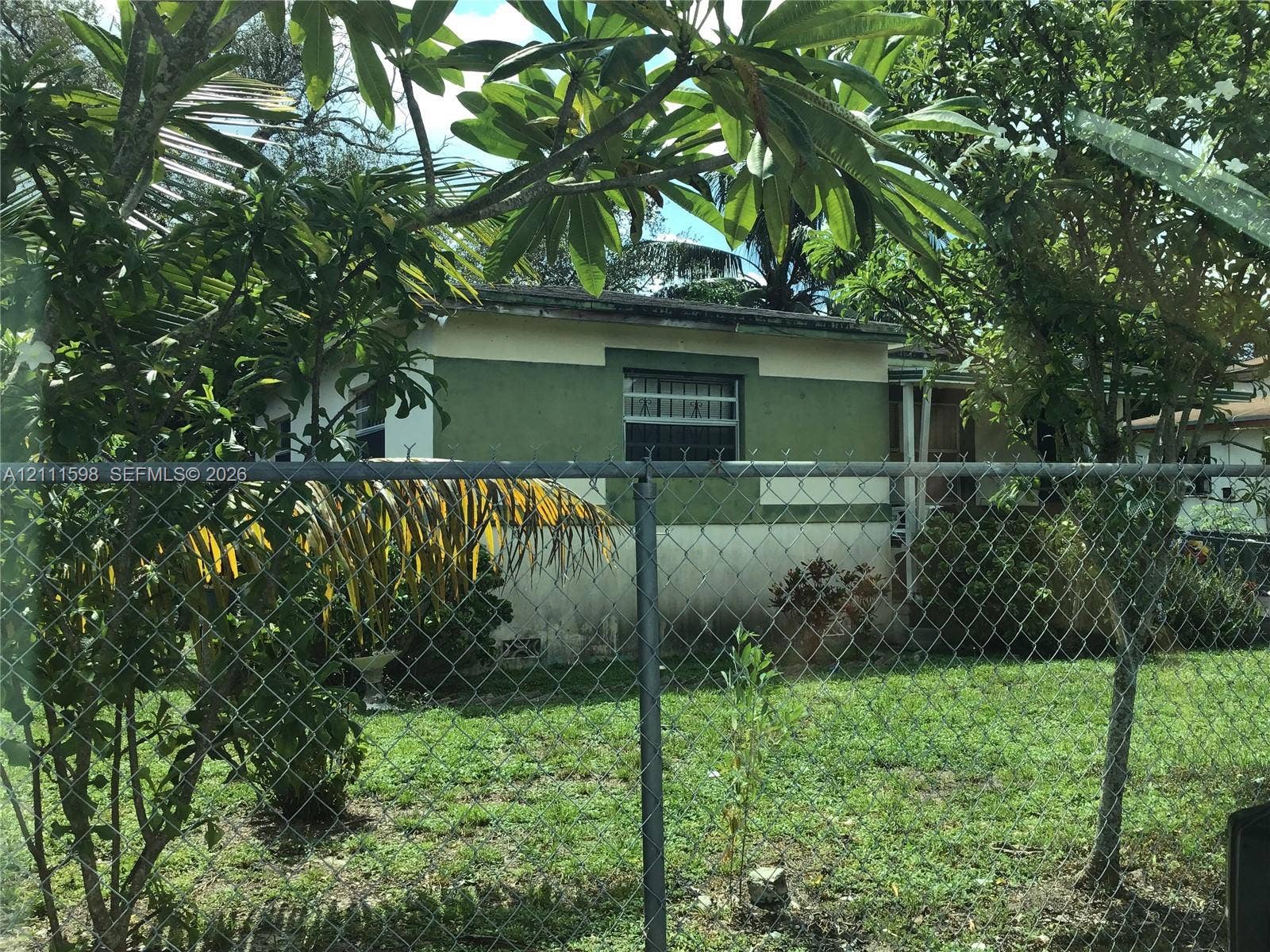 Single-story residence featuring a two-tone exterior facade, metal window security bars, and a chain-link perimeter fence