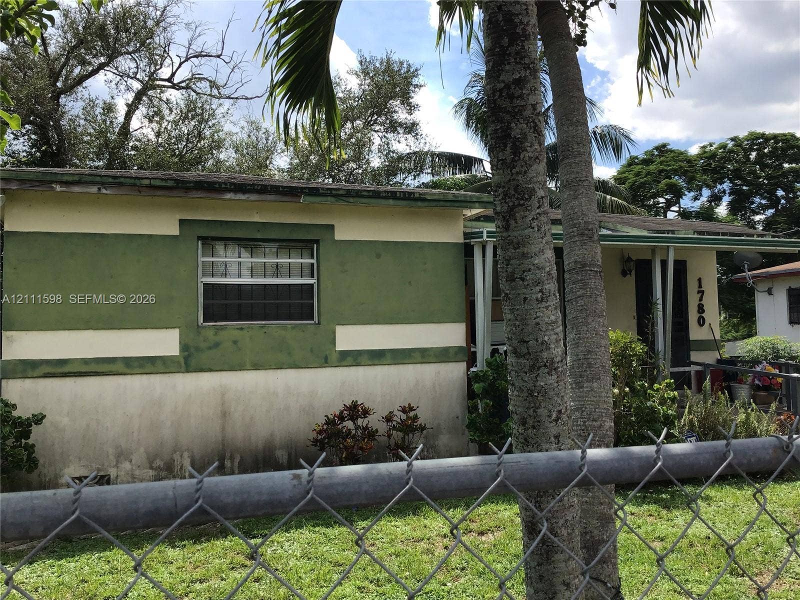 Single-story exterior featuring a painted stucco facade, metal-framed windows, a covered front entryway, and mature palm trees
