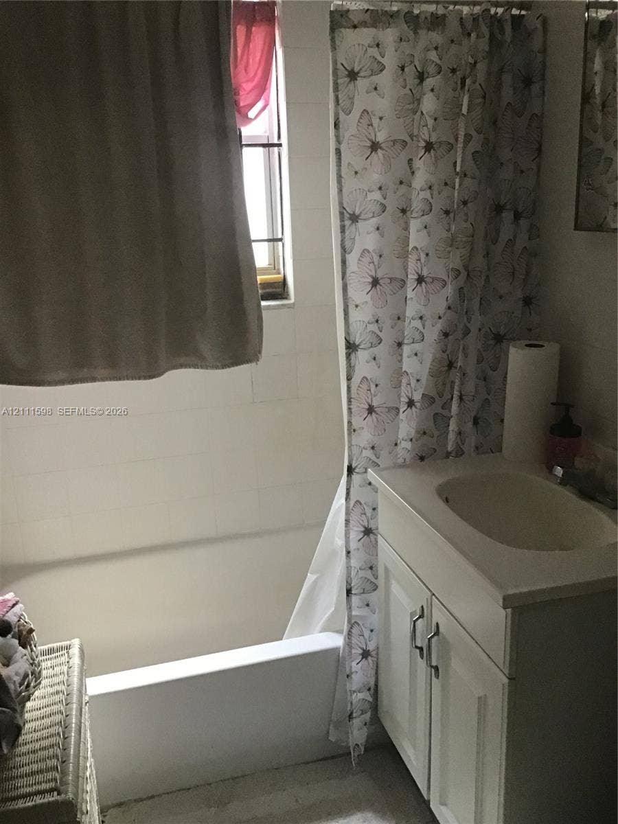 Bathroom featuring a porcelain tub with white tiled wall surround, single-basin vanity with cabinet storage, and window with muntins