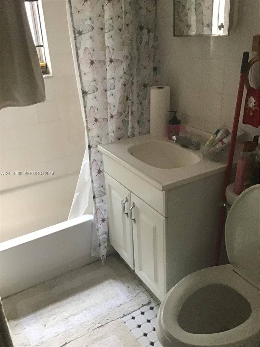 Bathroom featuring a white vanity cabinet with a stone-top integrated sink, a built-in shower and tub combination, white wall tiling, and black-and-white mosaic tile flooring