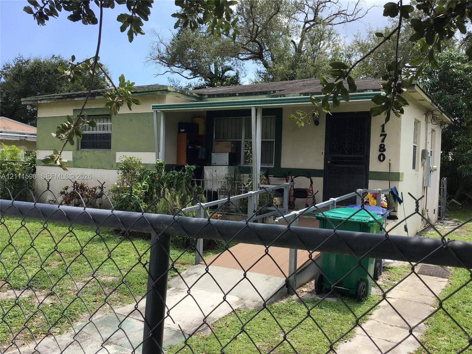Single-story exterior featuring a front porch with a metal access ramp and chain-link fencing