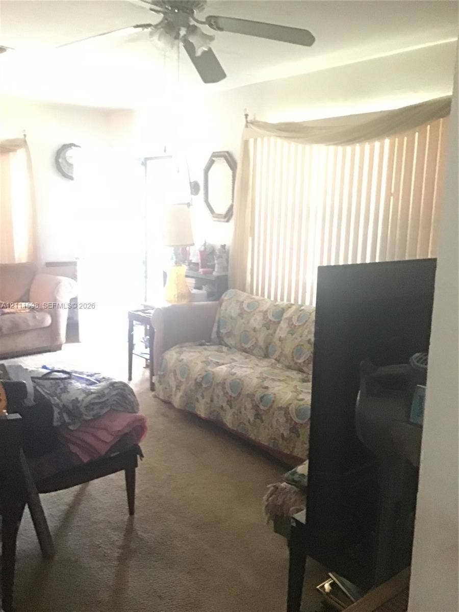Living area featuring a ceiling fan with integrated light fixture and large vertical window blinds