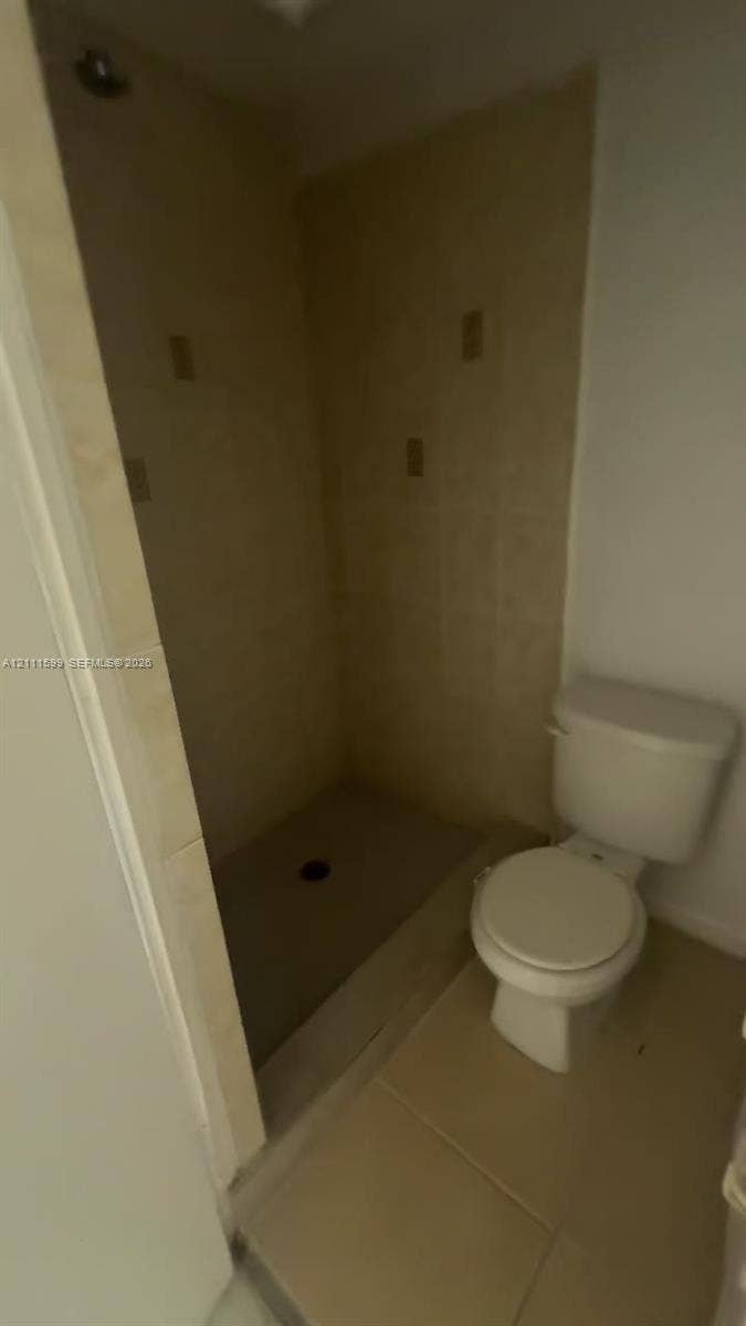 Walk-in shower with neutral tile surround, overhead shower head, and floor-mounted toilet