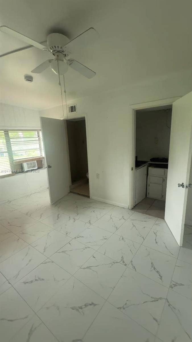 Large-format tile flooring with marble-style veining, four-blade ceiling fan, horizontal slat window blinds, and dual interior doorways