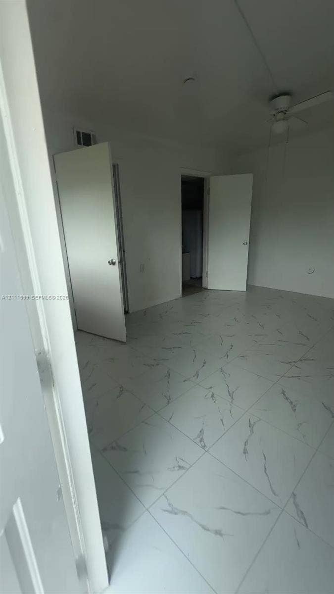 Large-format tile flooring with a white finish and grey veining, ceiling fan with integrated lighting, and white interior doors