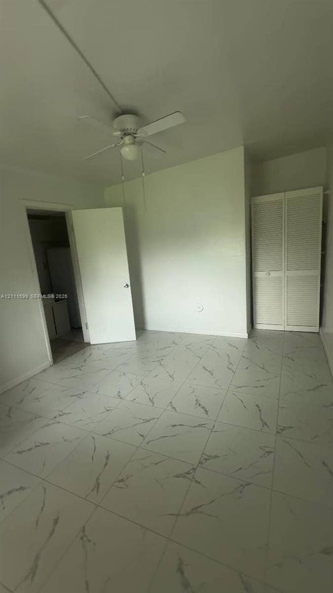 Large-format tile flooring with veining detail, ceiling-mounted paddle fan, and bi-fold louvered closet doors