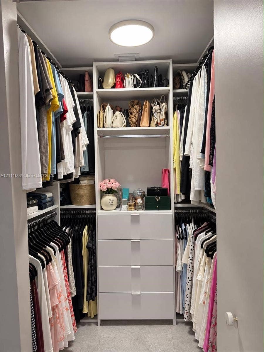 Walk-in closet featuring white built-in shelving, four integrated storage drawers with silver-tone pulls, multiple hanging rods, and a flush-mount overhead light fixture