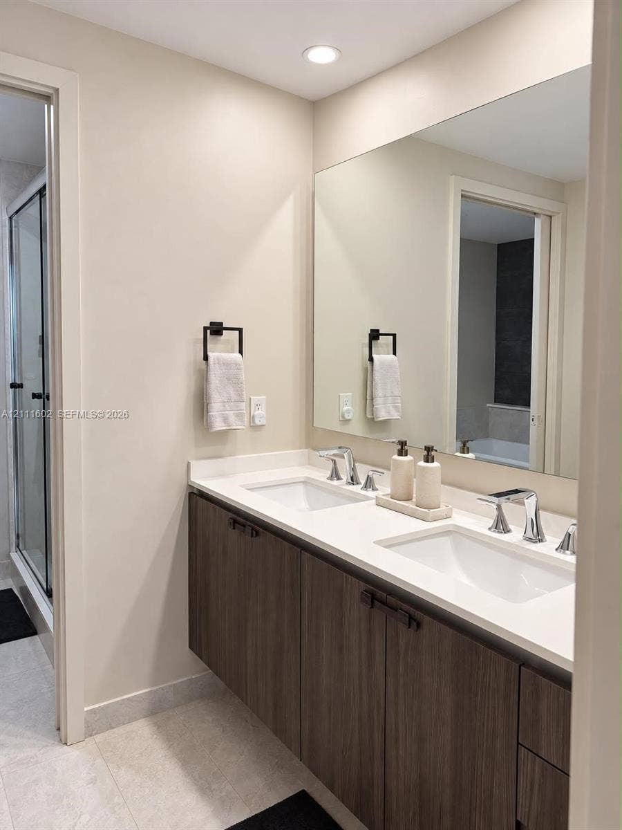 Floating wood-finish vanity with a double-sink white countertop, large wall-mounted mirror, matte black hardware, and recessed lighting