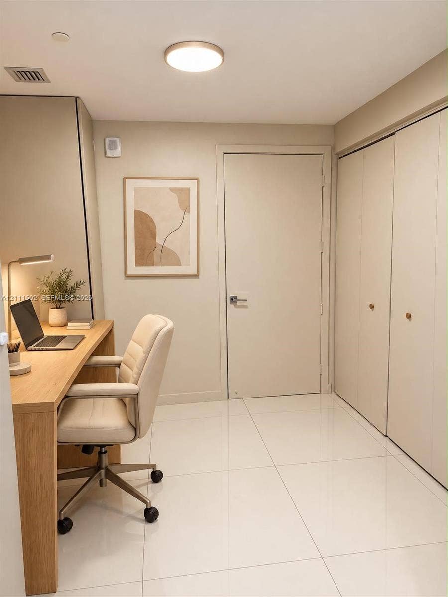 Built-in wood-finish desk, large-format tile flooring, flush-mount lighting, and floor-to-ceiling closets with brushed metal hardware