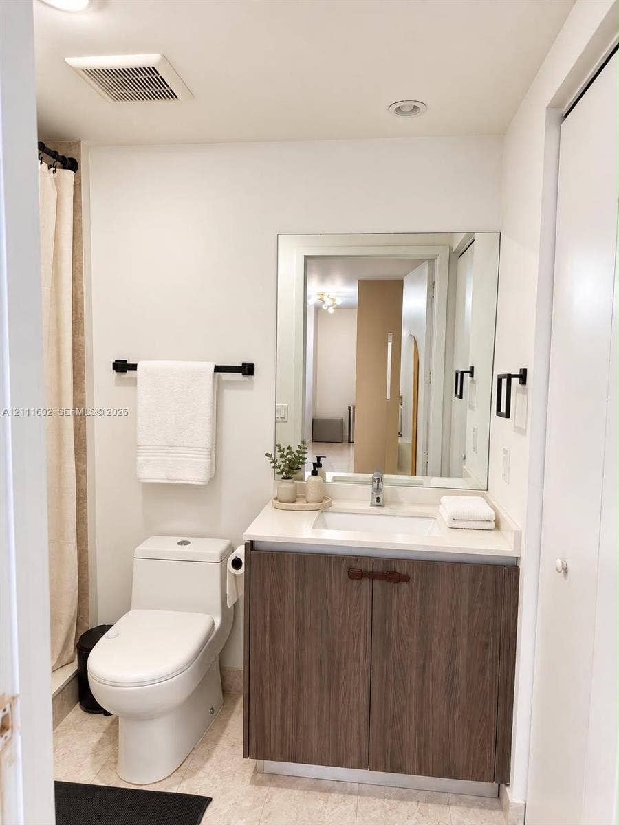Bathroom featuring a vanity with a wood-finish cabinet, solid surface countertop, integrated rectangular sink, wall-mounted mirror, and matte black hardware