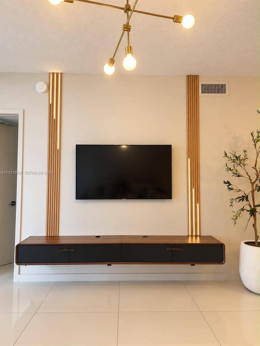 Wall-mounted floating media console featuring a two-tone wood and matte black finish, accented by vertical wood slat wall detailing with integrated lighting and a multi-arm modern brass pendant fixture
