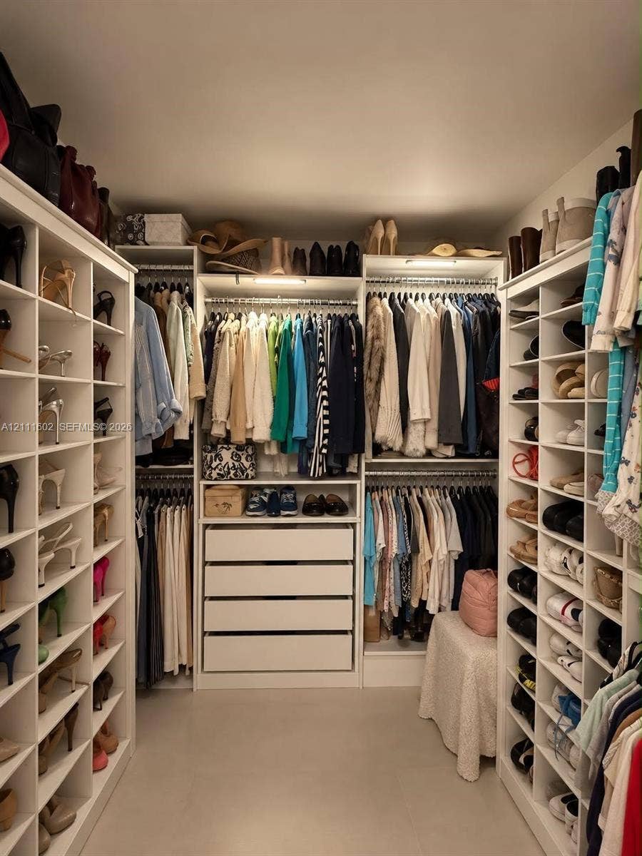 Walk-in closet featuring extensive built-in white shelving, multiple hanging rods, four deep storage drawers, and integrated overhead lighting