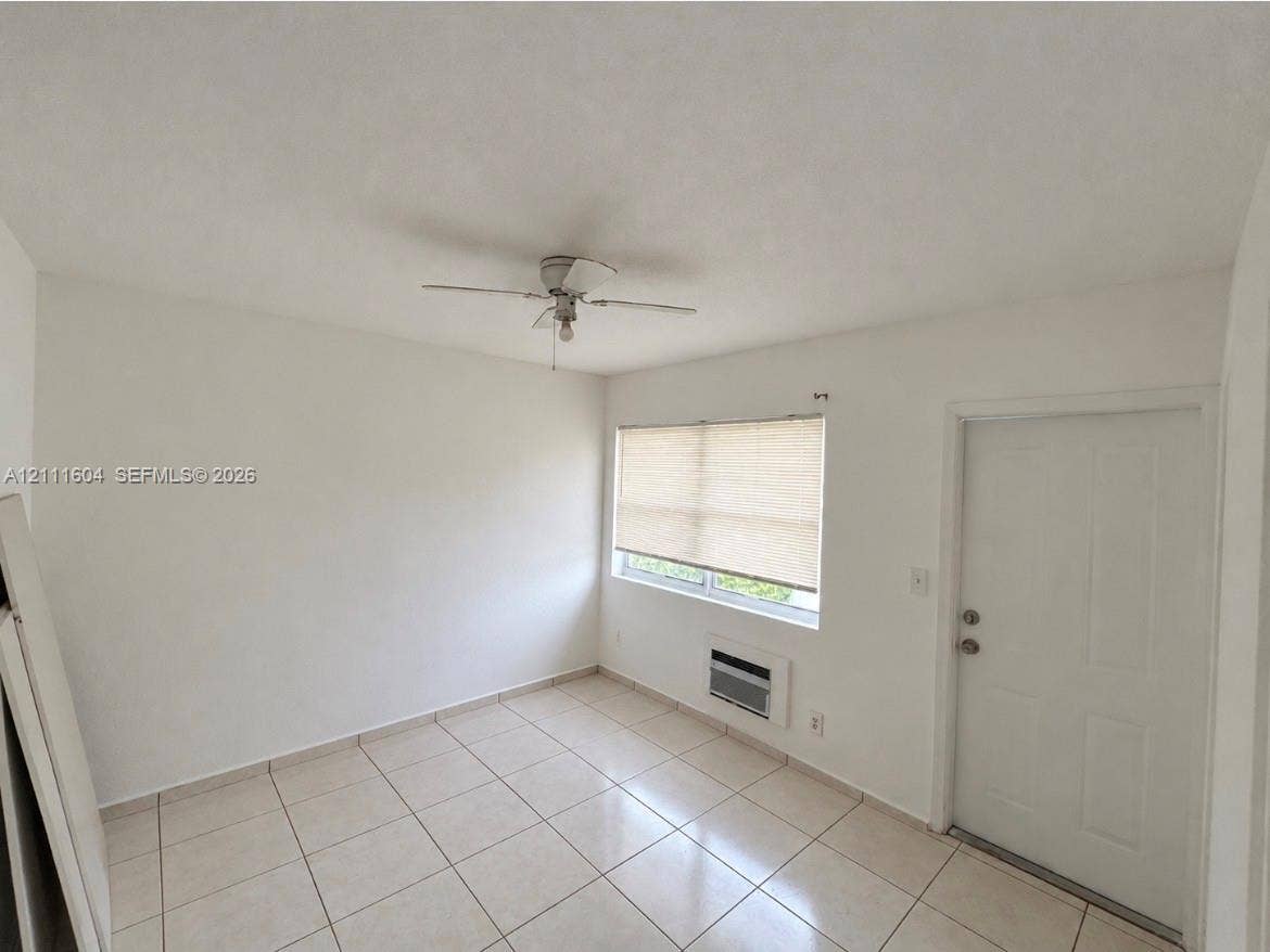 Room featuring neutral wall-to-wall ceramic tile flooring, a ceiling fan, and a wall-mounted climate control unit