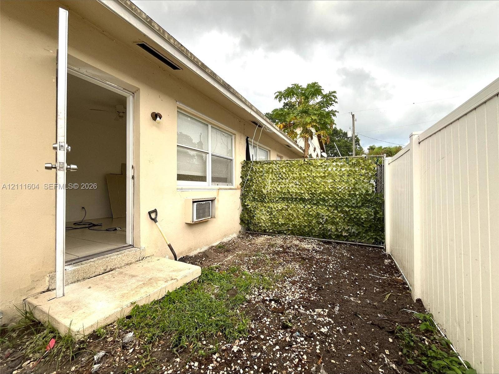 Exterior space featuring a concrete step, white vinyl privacy fencing, and a decorative foliage screen