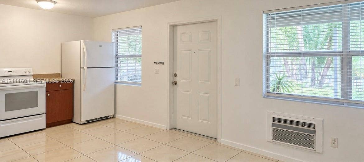 Kitchen space featuring ceramic tile flooring, neutral wall finishes, windows with horizontal blinds, built-in cabinetry, and a wall-mounted air conditioning unit