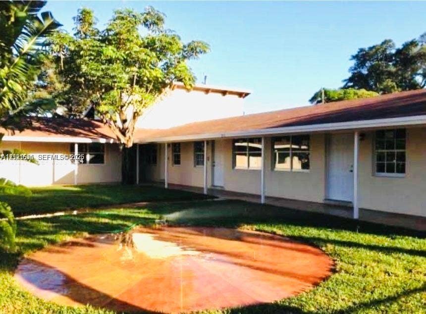 L-shaped exterior featuring a covered walkway, multi-pane windows, a central circular hardscape patio, and mature trees