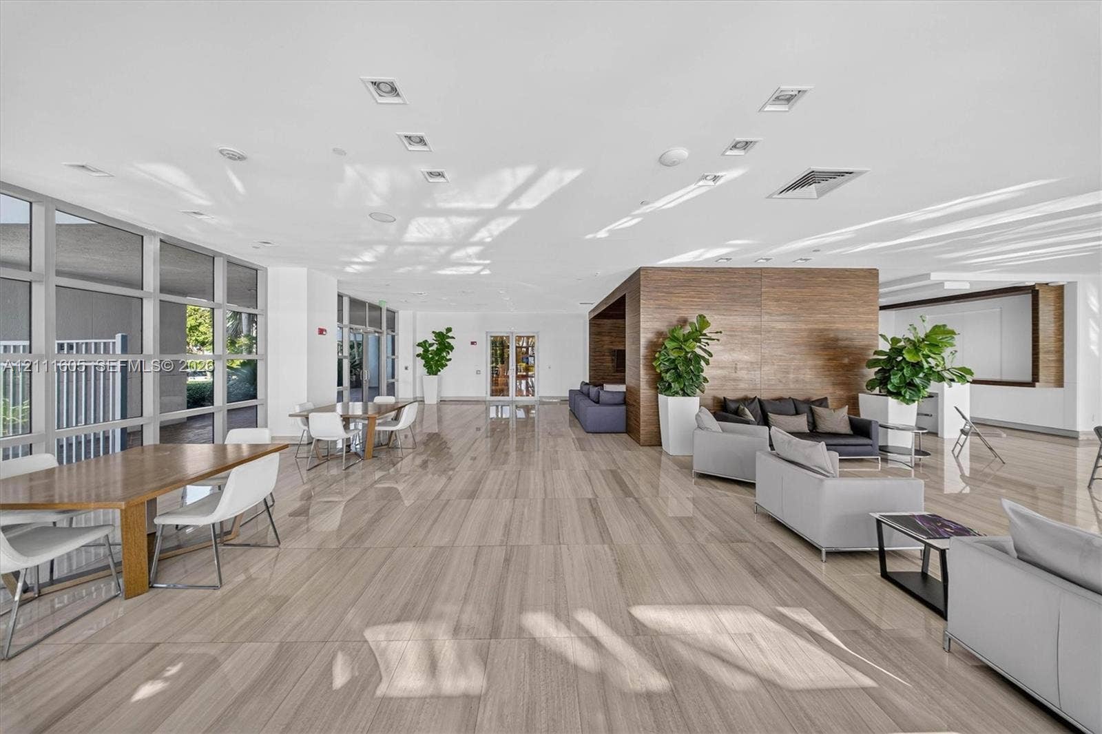 Spacious communal area featuring large-format stone-finish flooring, full-height glass window panels, and a prominent wood-panel accent wall with integrated recessed lighting