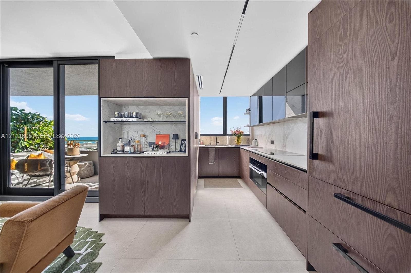 Kitchen featuring flat-panel wood-finish cabinetry, integrated appliances, stone backsplash, built-in dry bar, and large-format tile flooring