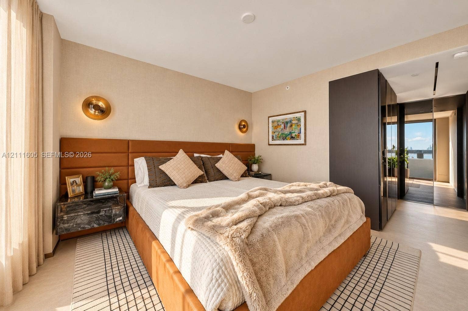 Neutral-toned room featuring a built-in upholstered headboard, metallic wall-mounted sconces, and dark floor-to-ceiling built-in cabinetry