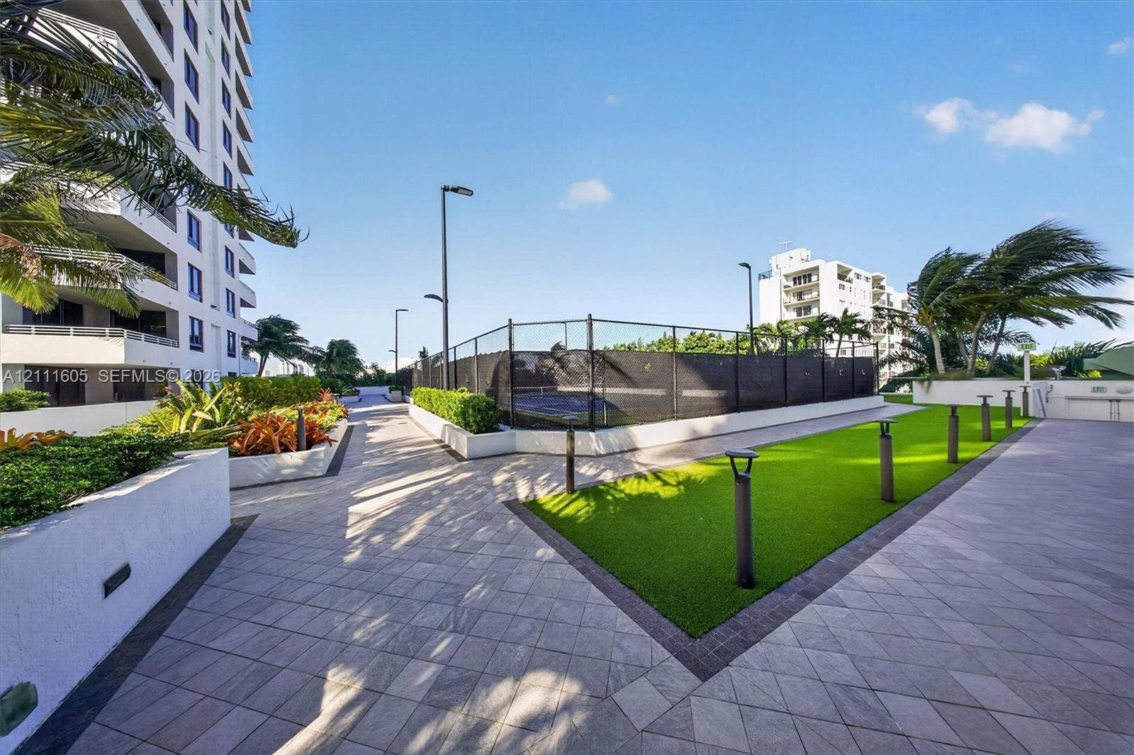 Aerial perspective of a high-rise residential building featuring a landscaped podium terrace with a circular water feature, a kidney-shaped ground-level swimming pool, and direct proximity to the waterfront