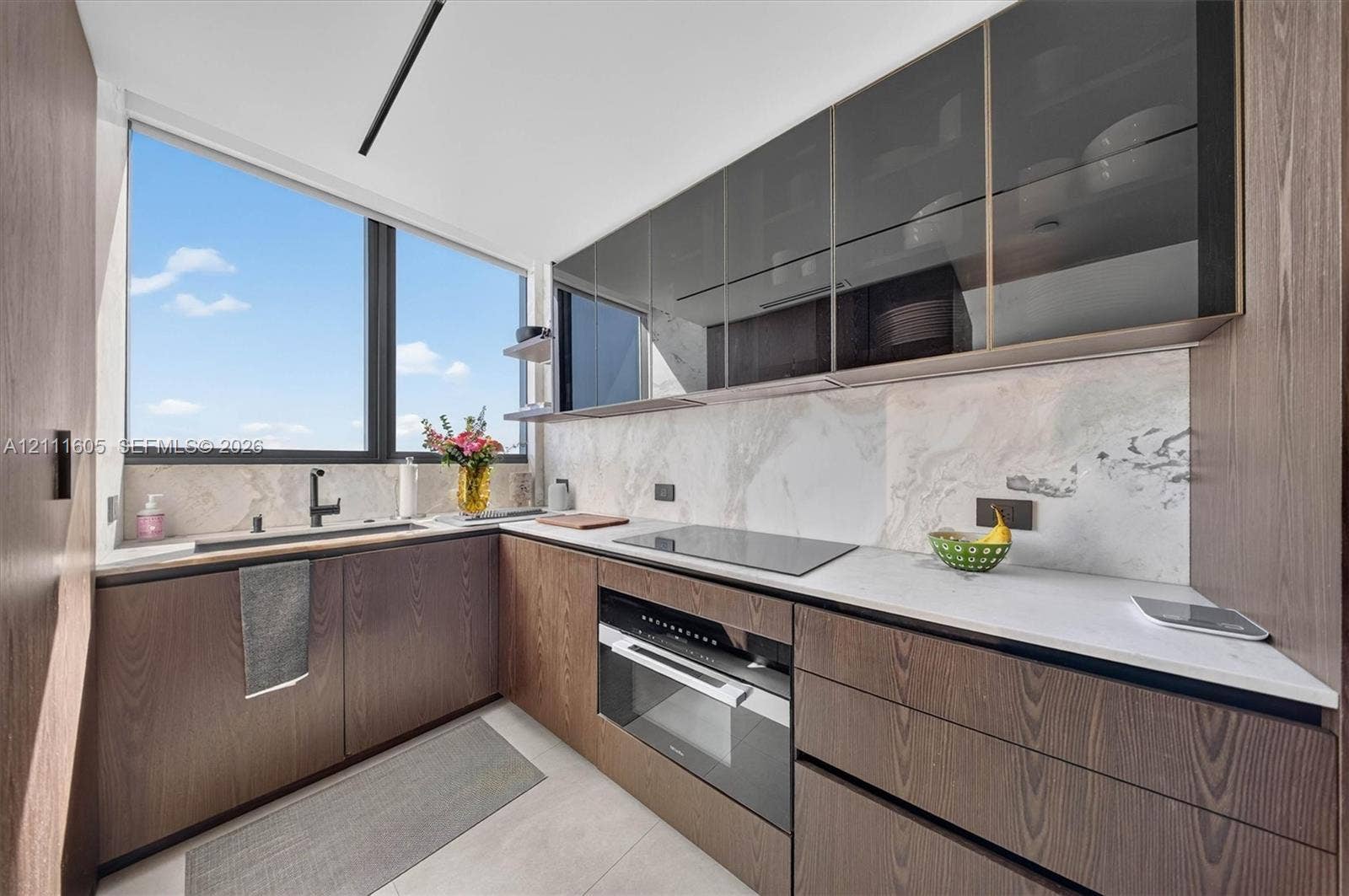 Kitchen featuring wood-finish cabinetry, stone-patterned backsplash, light-colored countertops, integrated cooktop and oven, and upper glass-front cabinets