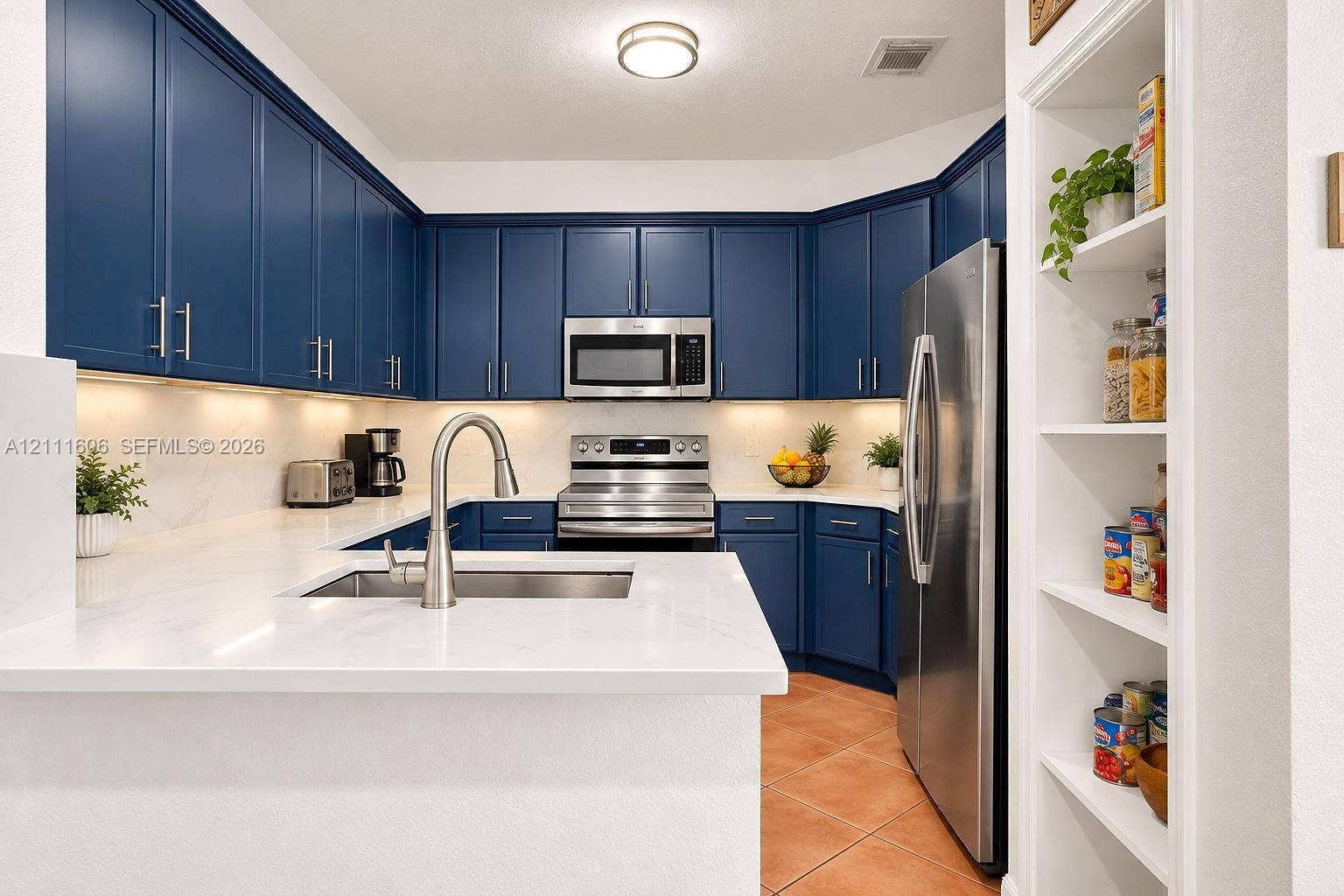 Kitchen featuring navy cabinetry, solid surface countertops, stainless steel appliances, under-cabinet lighting, and built-in shelving