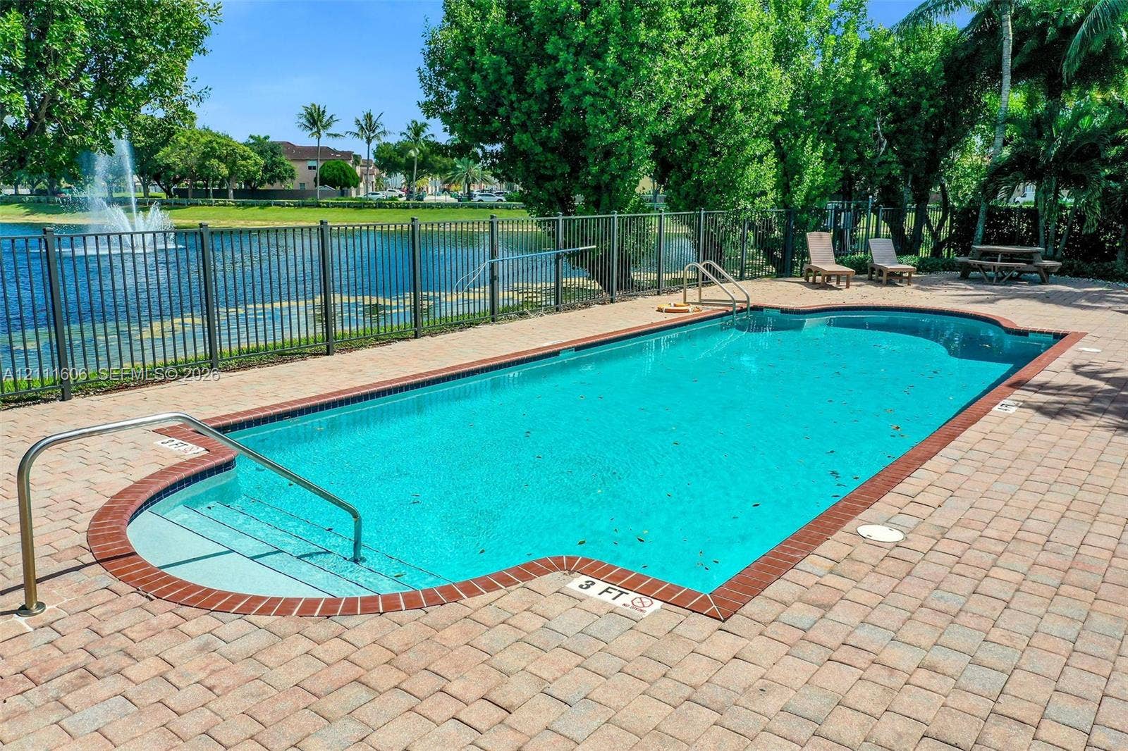 In-ground swimming pool with brick paver decking, metal perimeter fencing, and stainless steel handrails
