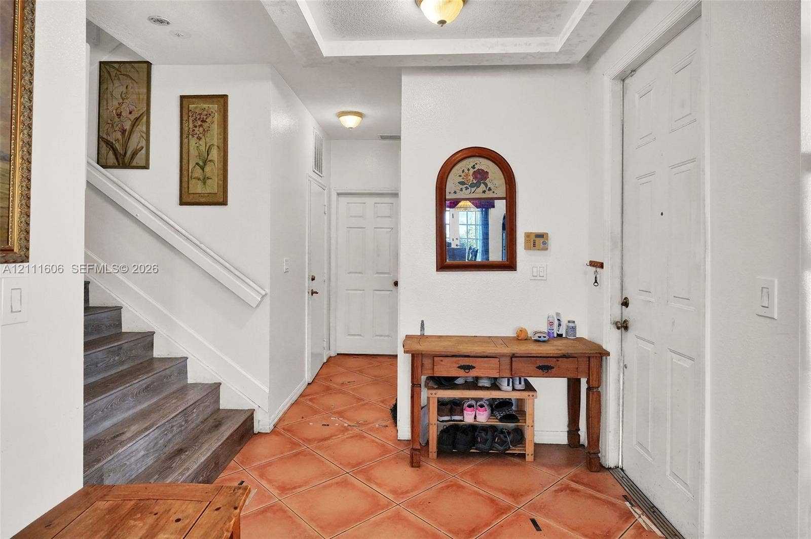 Foyer featuring terracotta tile flooring, recessed tray ceiling, built-in staircase with wood-finish treads, and arched wall-mounted mirror