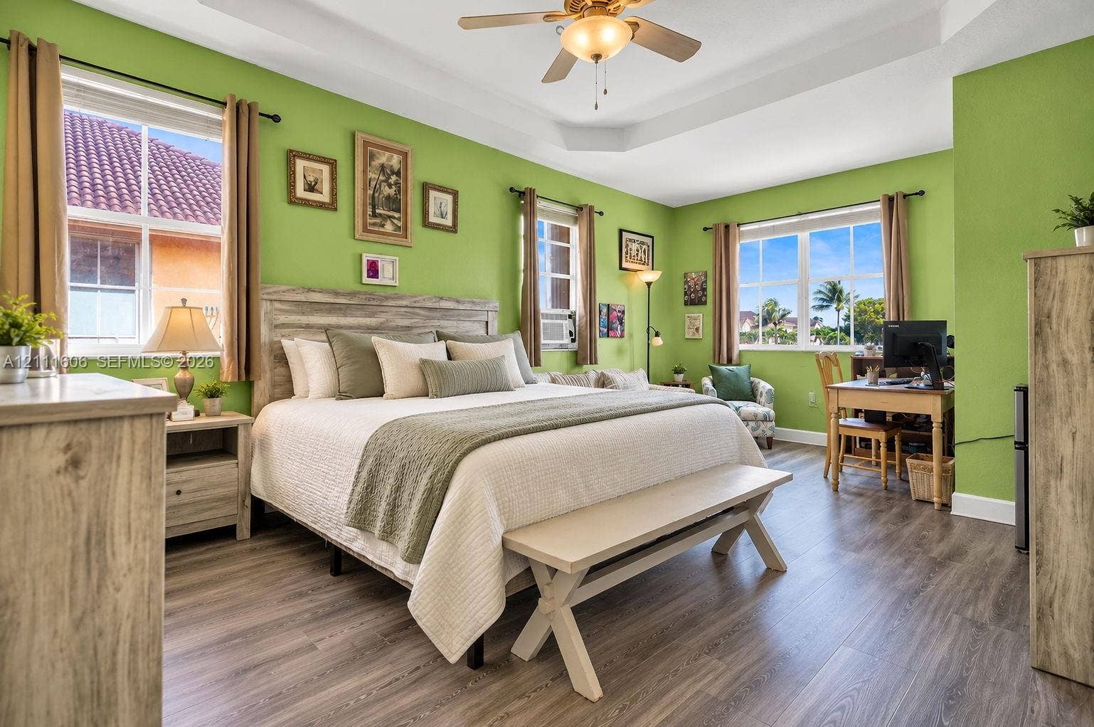 Tray ceiling featuring a central lighted ceiling fan, wood-finish flooring, and multiple large windows