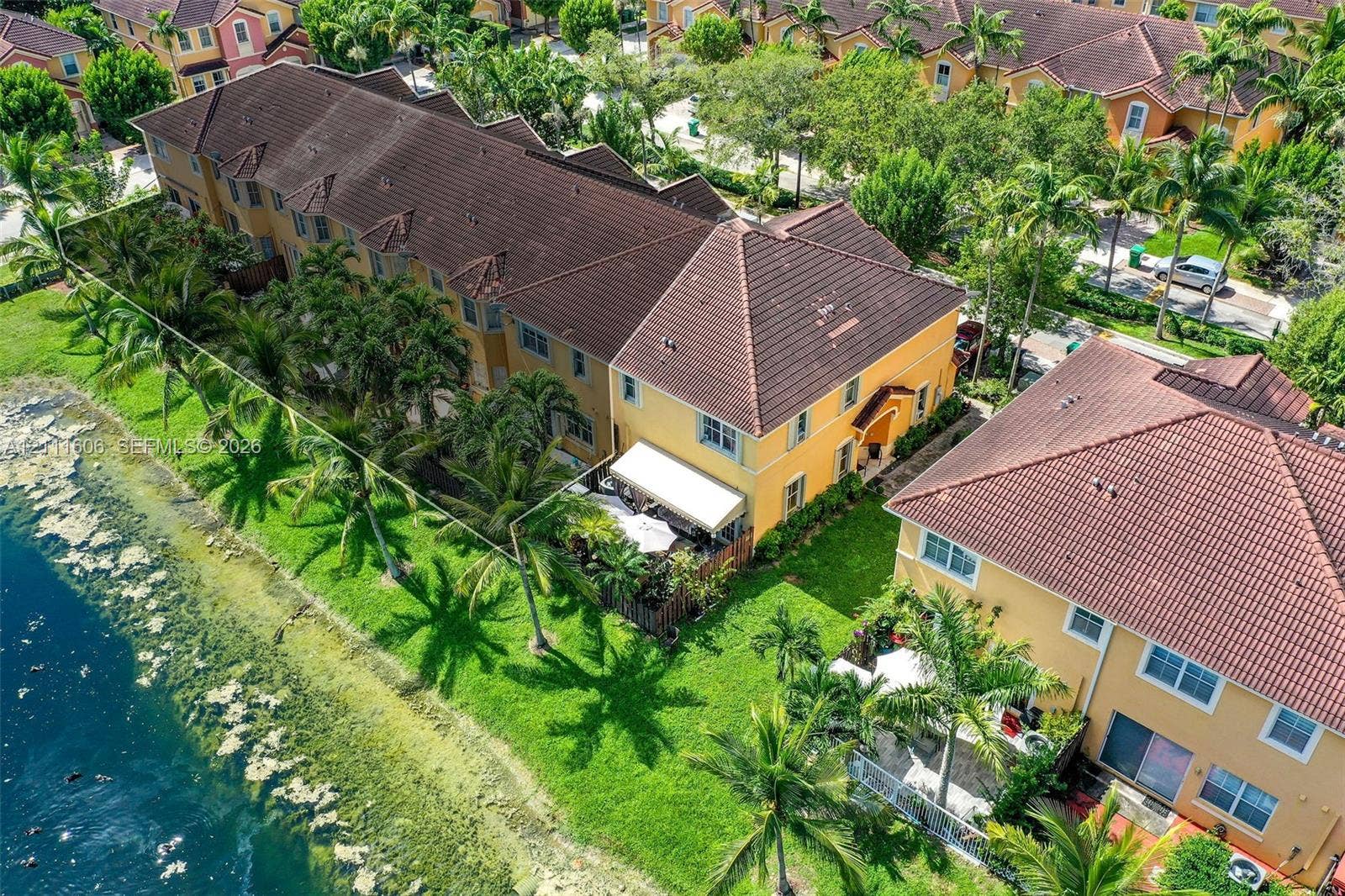 Waterfront residence featuring a tile roof, stucco exterior, rear patio, and established tropical landscaping