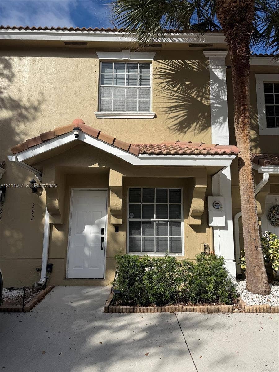 Exterior facade featuring a concrete tile roof, stucco finish, decorative corbel brackets at the entryway, and multi-pane grid windows