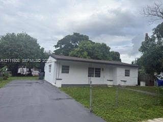 Single-story exterior featuring a white masonry facade, horizontal roofline, long concrete driveway, and front lawn
