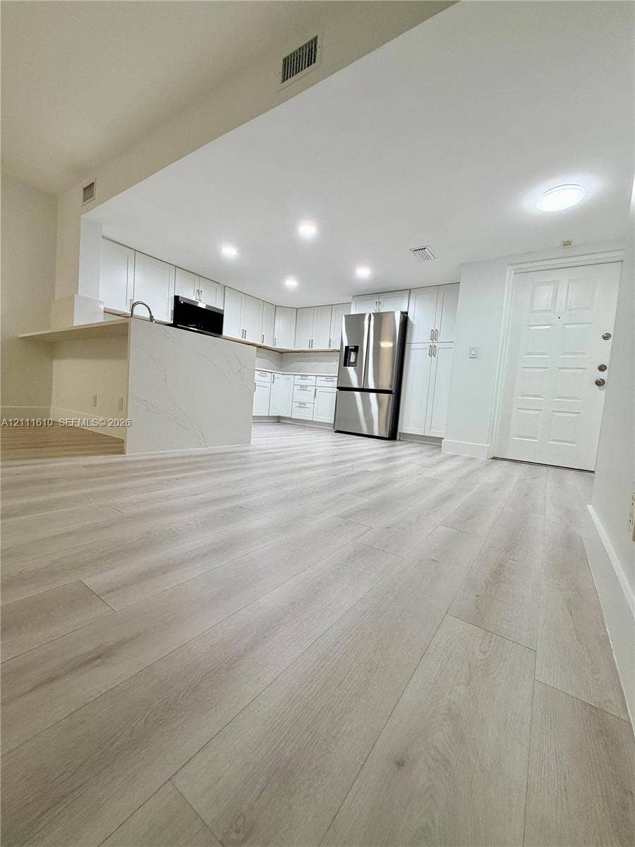 Kitchen featuring white cabinetry, wood-finish flooring, stone-patterned waterfall island, stainless steel refrigerator, and recessed lighting