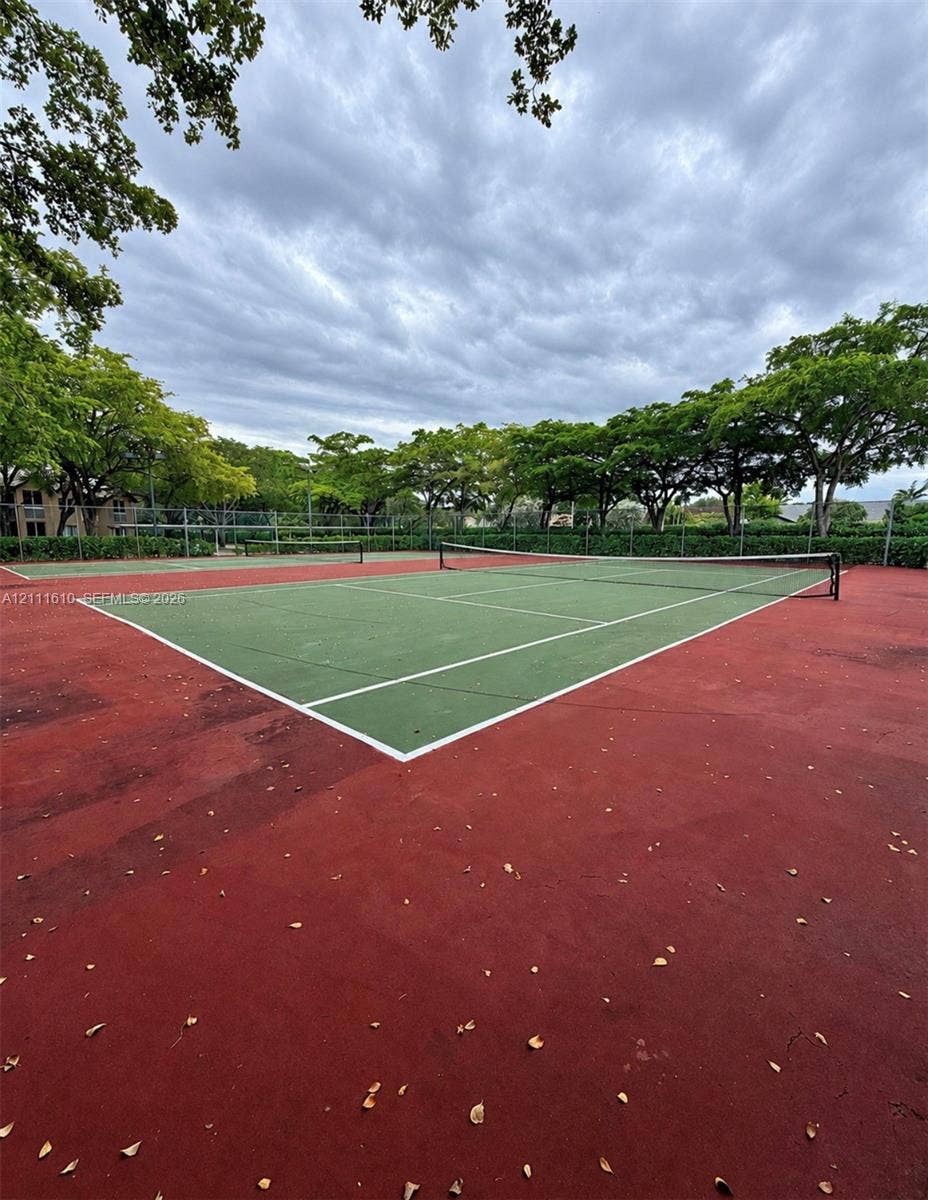 Dual tennis courts featuring a synthetic hard-court surface, perimeter chain-link fencing, and mature trees