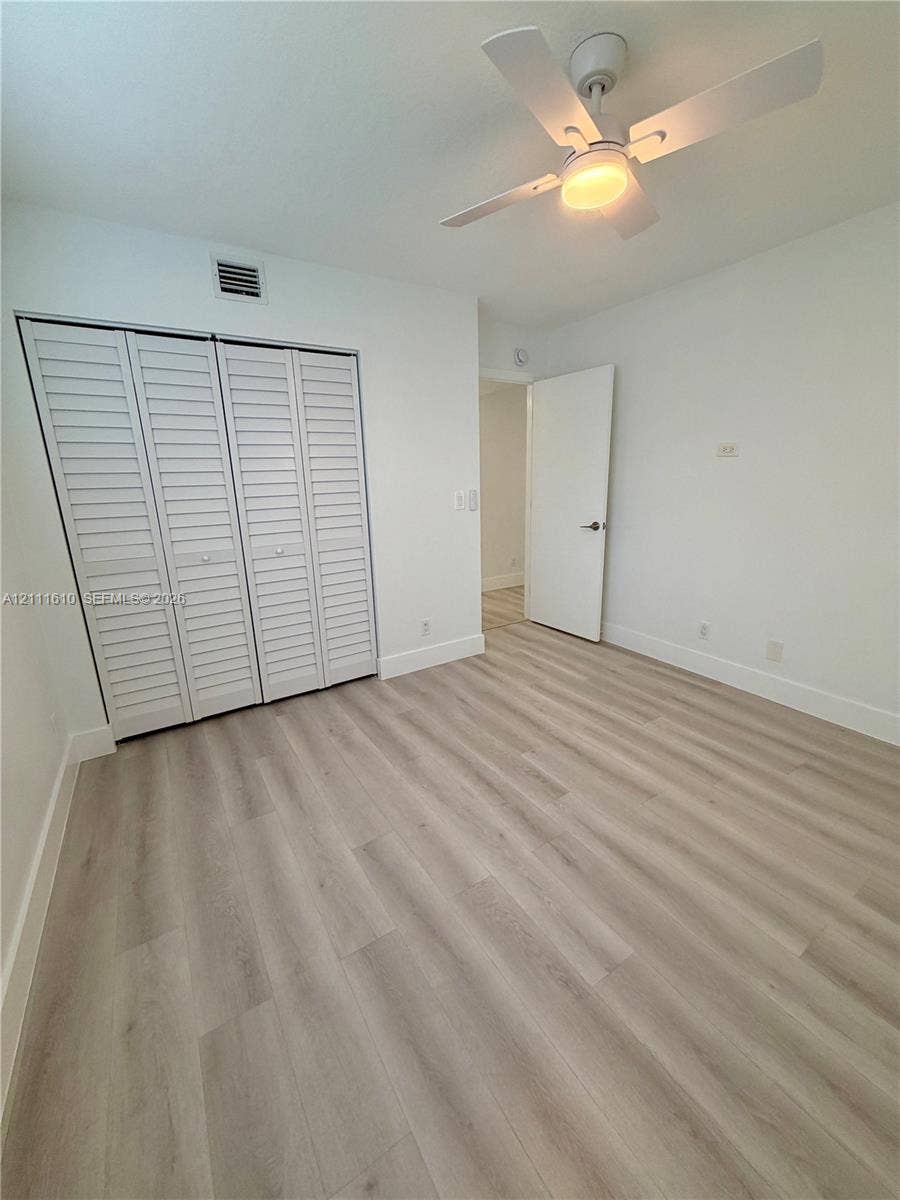 Wood-finish flooring, white louvered-style closet doors, and an integrated ceiling fan with light fixture