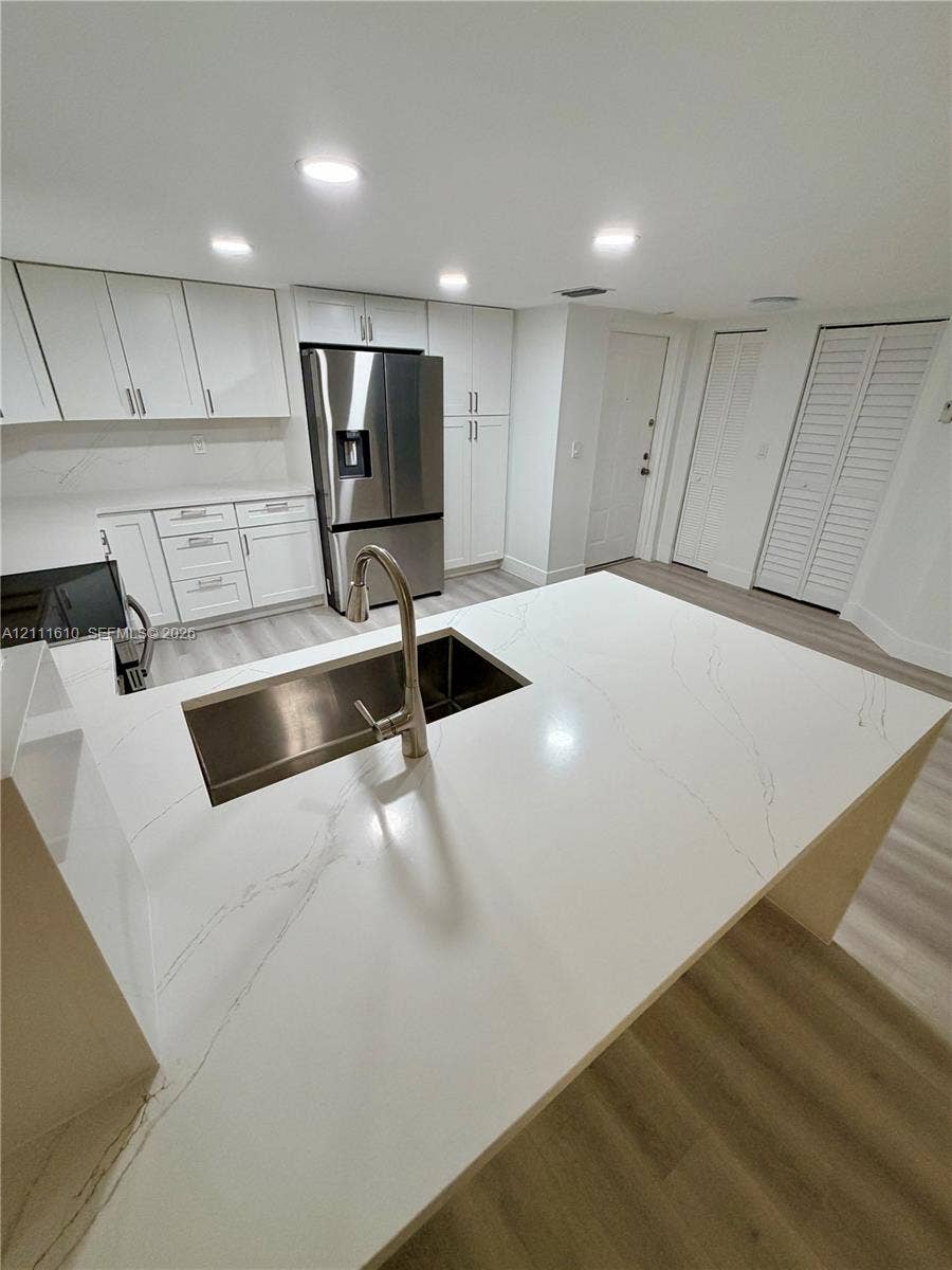 Kitchen featuring a central island with a solid surface countertop, undermount stainless steel sink, pull-down faucet, white cabinetry, and stainless steel refrigerator