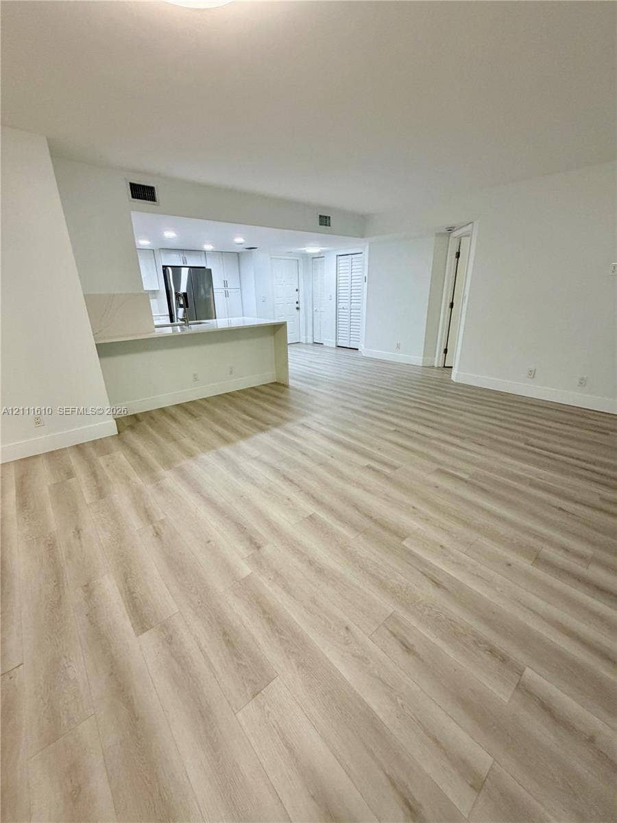 Open-concept interior featuring light-toned wood-finish flooring, a kitchen breakfast bar with solid-surface countertops, white cabinetry, and louvered closet doors