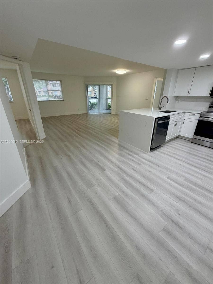 Kitchen featuring white cabinetry, quartz countertops, stainless steel appliances, and a peninsula, complemented by wood-finish flooring