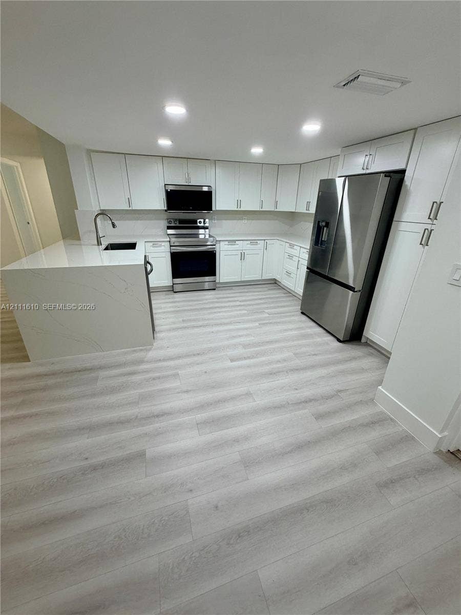 Kitchen featuring white cabinetry, quartz countertops with waterfall edge, wood-finish flooring, and stainless steel appliances