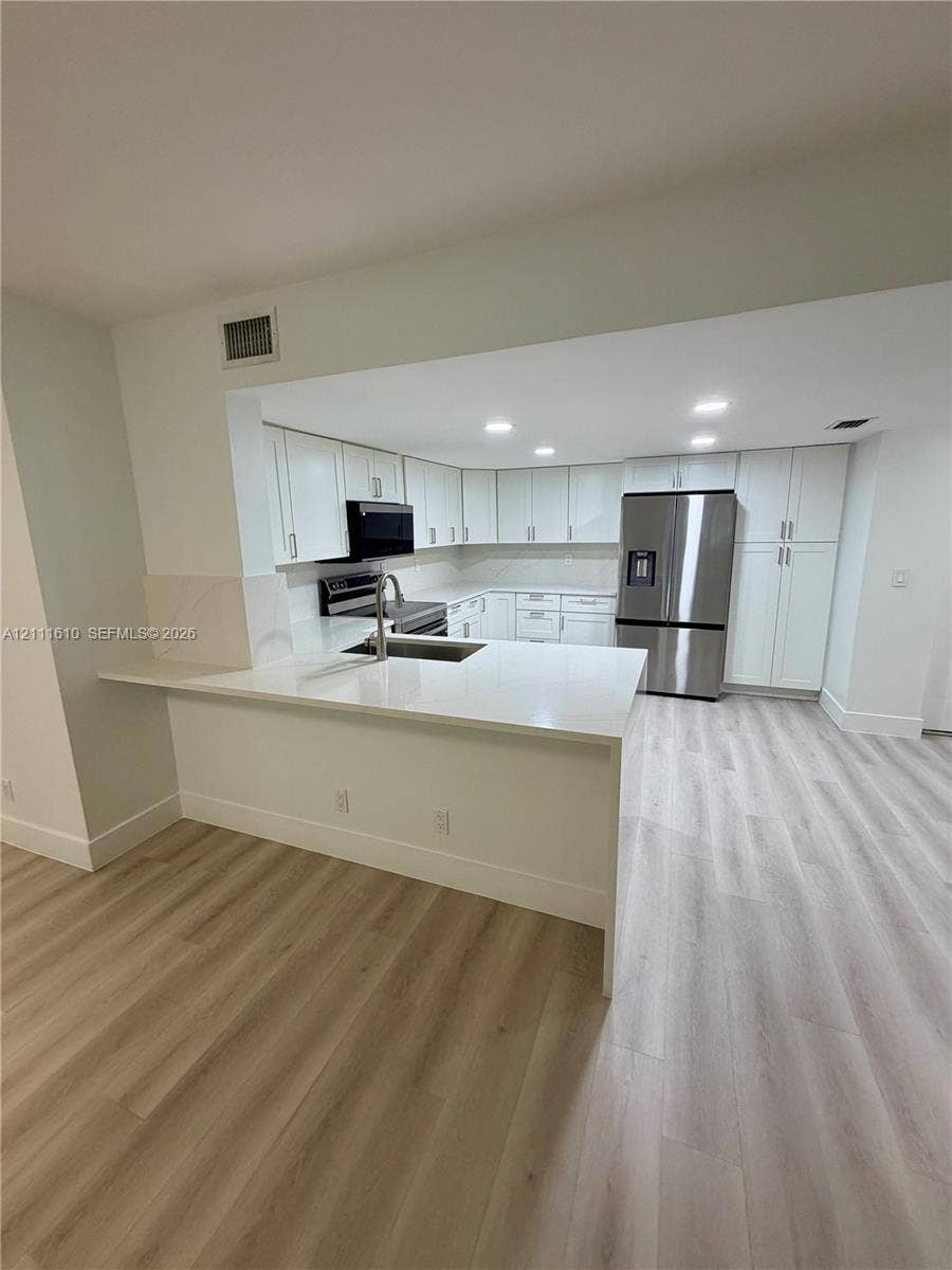 Kitchen featuring white shaker-style cabinetry, quartz countertops, a peninsula with an undermount stainless steel sink, recessed lighting, and wood-finish flooring