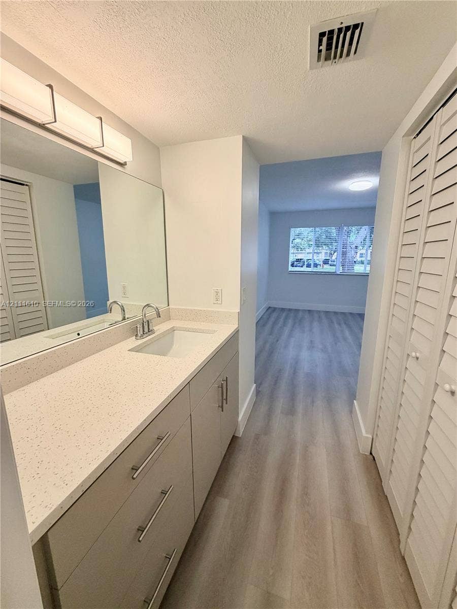Bathroom vanity featuring a speckled solid-surface countertop, an integrated rectangular sink, brushed-metal hardware, large wall-mounted mirror, and wood-finish flooring throughout the space