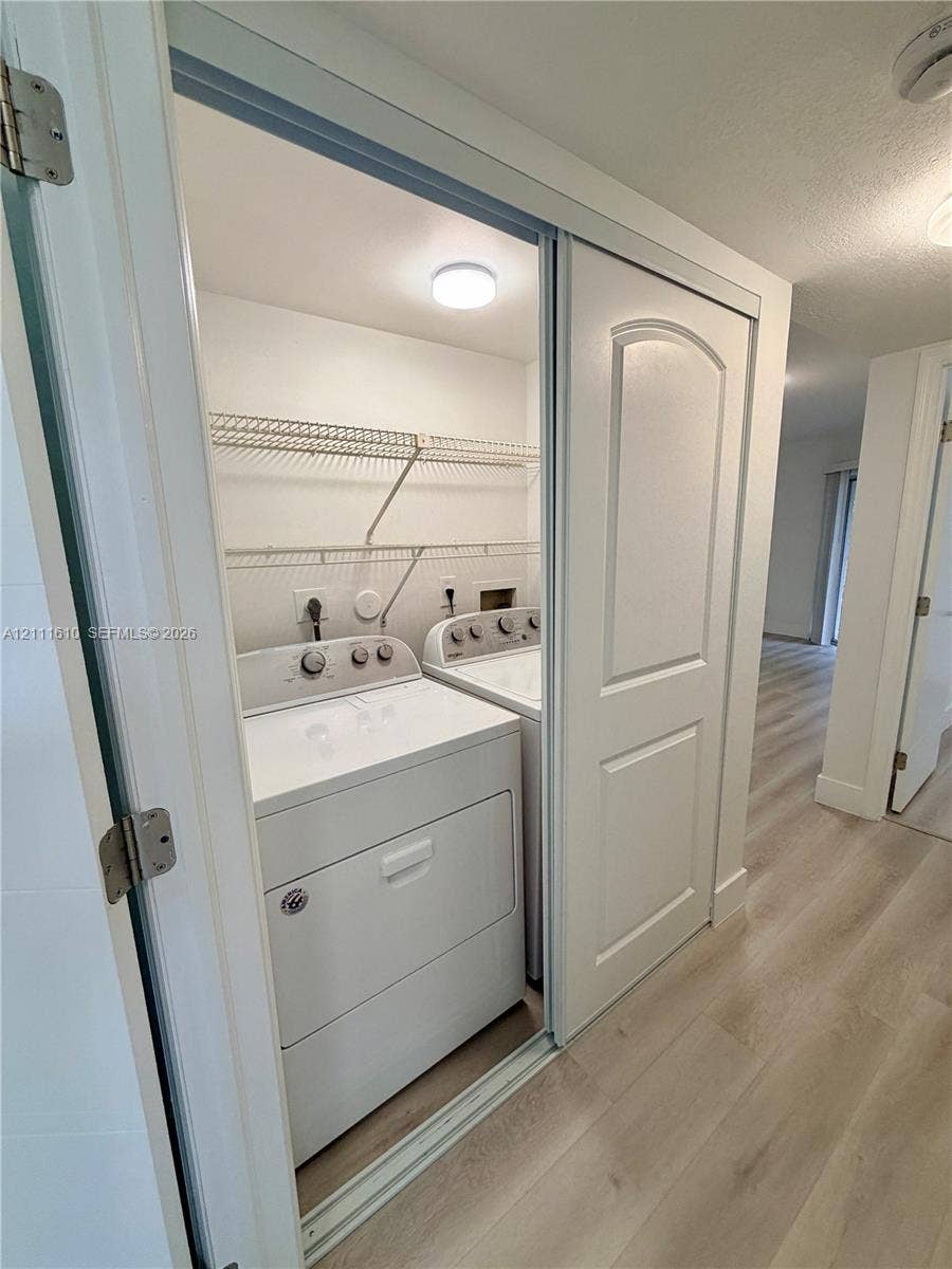 Laundry closet featuring built-in wire shelving and sliding panel doors, set against wood-finish flooring
