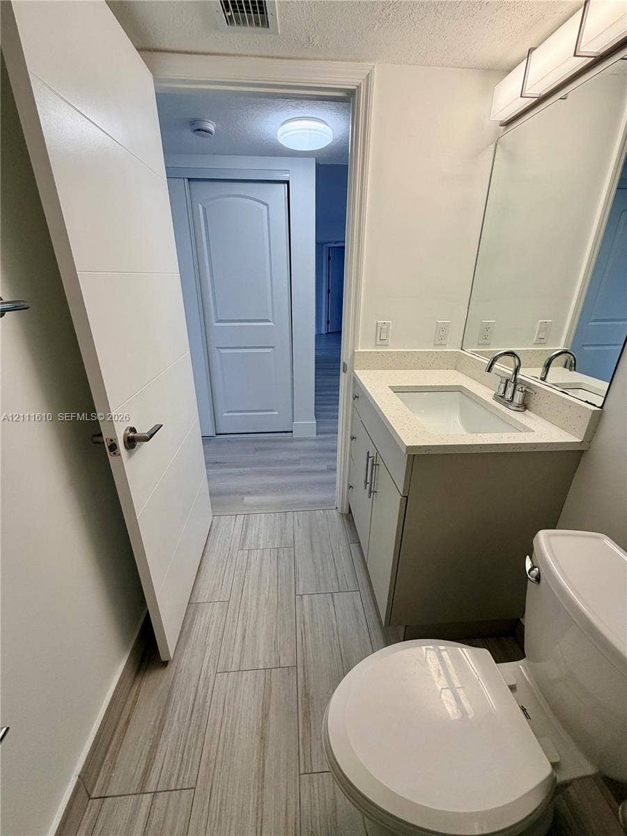 Bathroom featuring a vanity with a light-toned countertop, integrated basin, sleek cabinet hardware, and wood-finish tile flooring