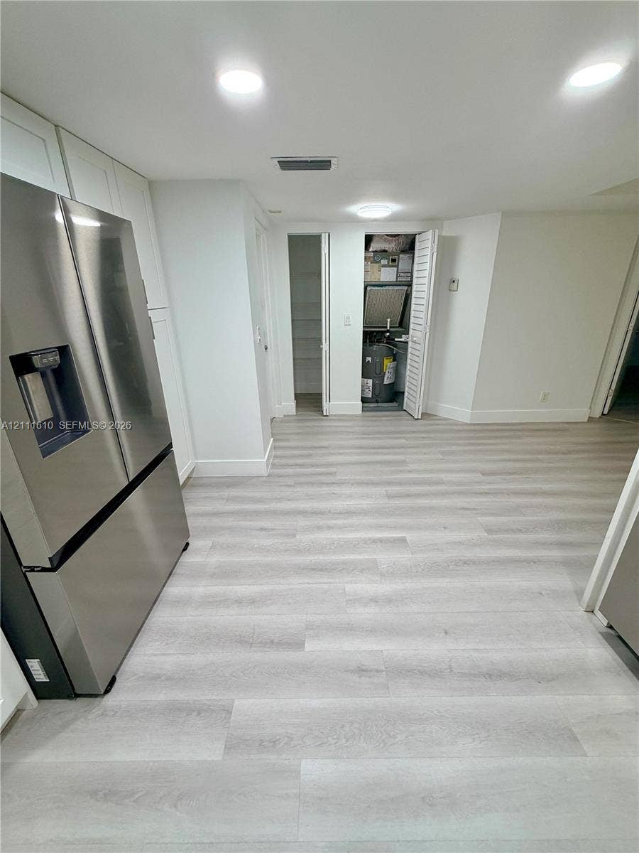 Light-toned wood-finish flooring, stainless steel French door refrigerator, recessed ceiling lighting, and built-in closet storage