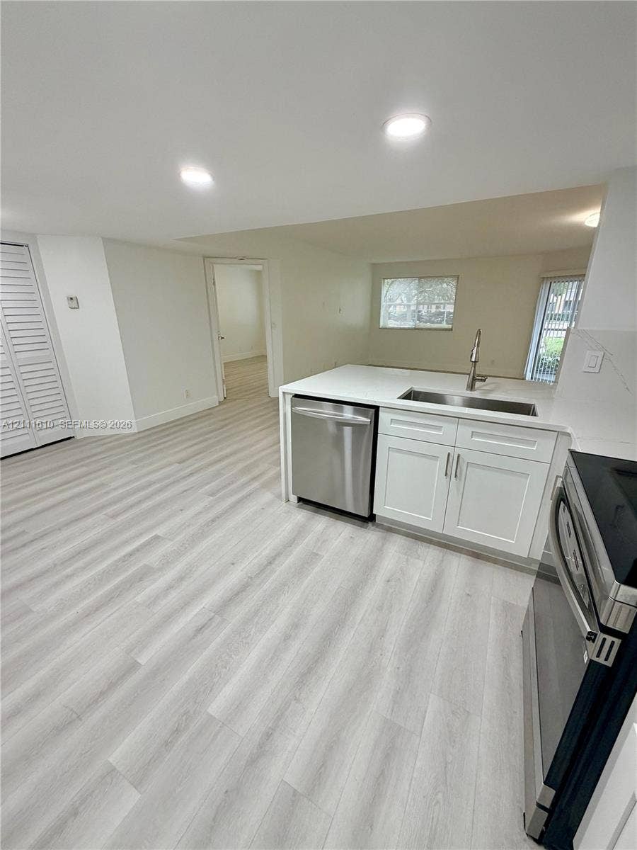 Kitchen area featuring wood-finish flooring, white cabinetry, solid-surface countertops, stainless steel appliances, and recessed lighting