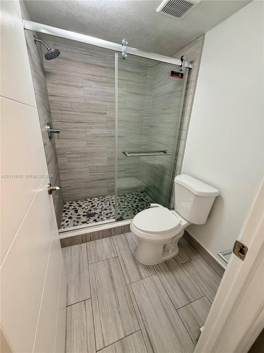 Walk-in shower featuring a sliding glass door, multi-textured stone tile flooring, horizontal wall tiling, and a fixed shower head