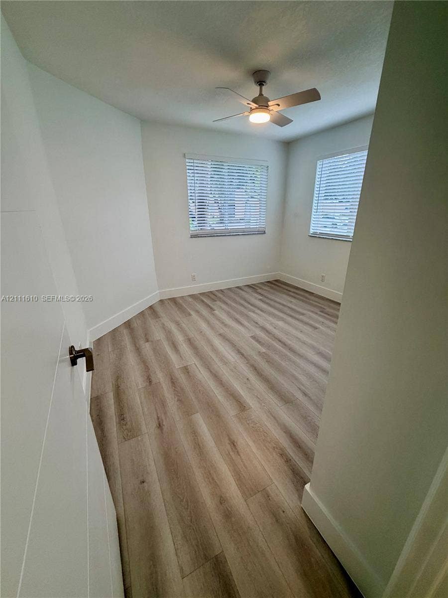 Room featuring wood-finish flooring, dual windows with fitted blinds, and a central ceiling fan with an integrated light fixture